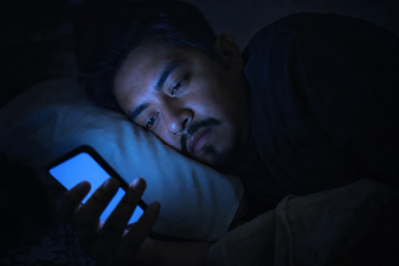 Persona viendo la pantalla del celular a oscuras con la luz azul dándole en la cara